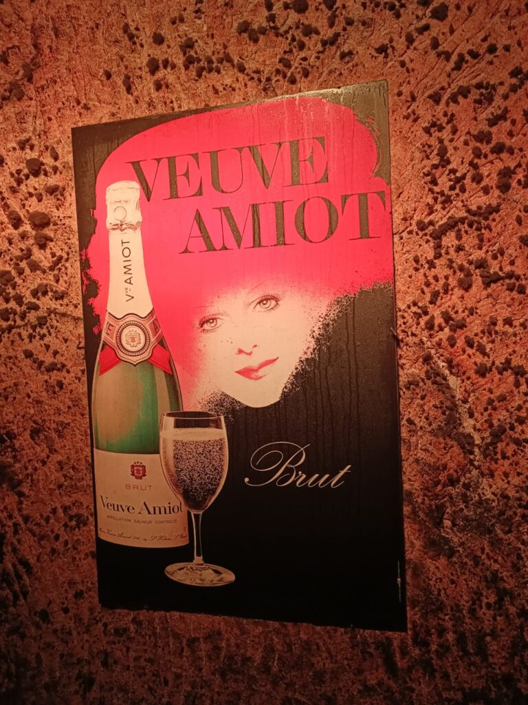 Affiche vintage Veuve Amiot dans les caves troglodytiques de Saumur, symbole du patrimoine viticole local.